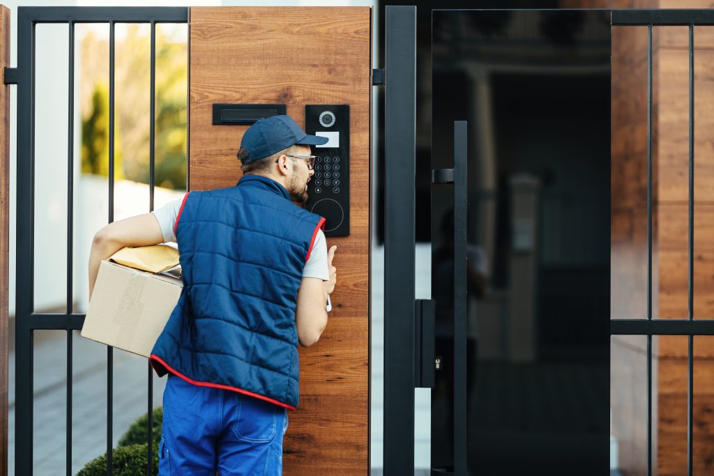 Rear view of a courier ringing on customer's intercom while maki